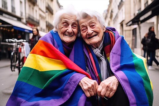 Zwei ältere Frauen schwenken stolz Regenbogenfahnen auf der Straße und nehmen die Herausforderungen und Chancen der LSBTIQ*-Community an.
